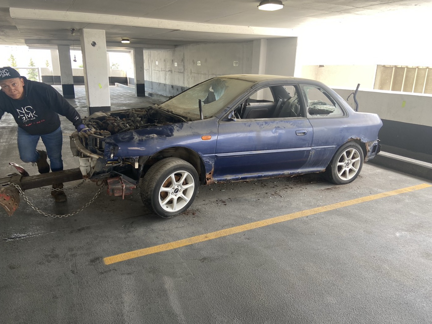 Blue GC8 Impreza sedan parts car being winched onto a tow truck