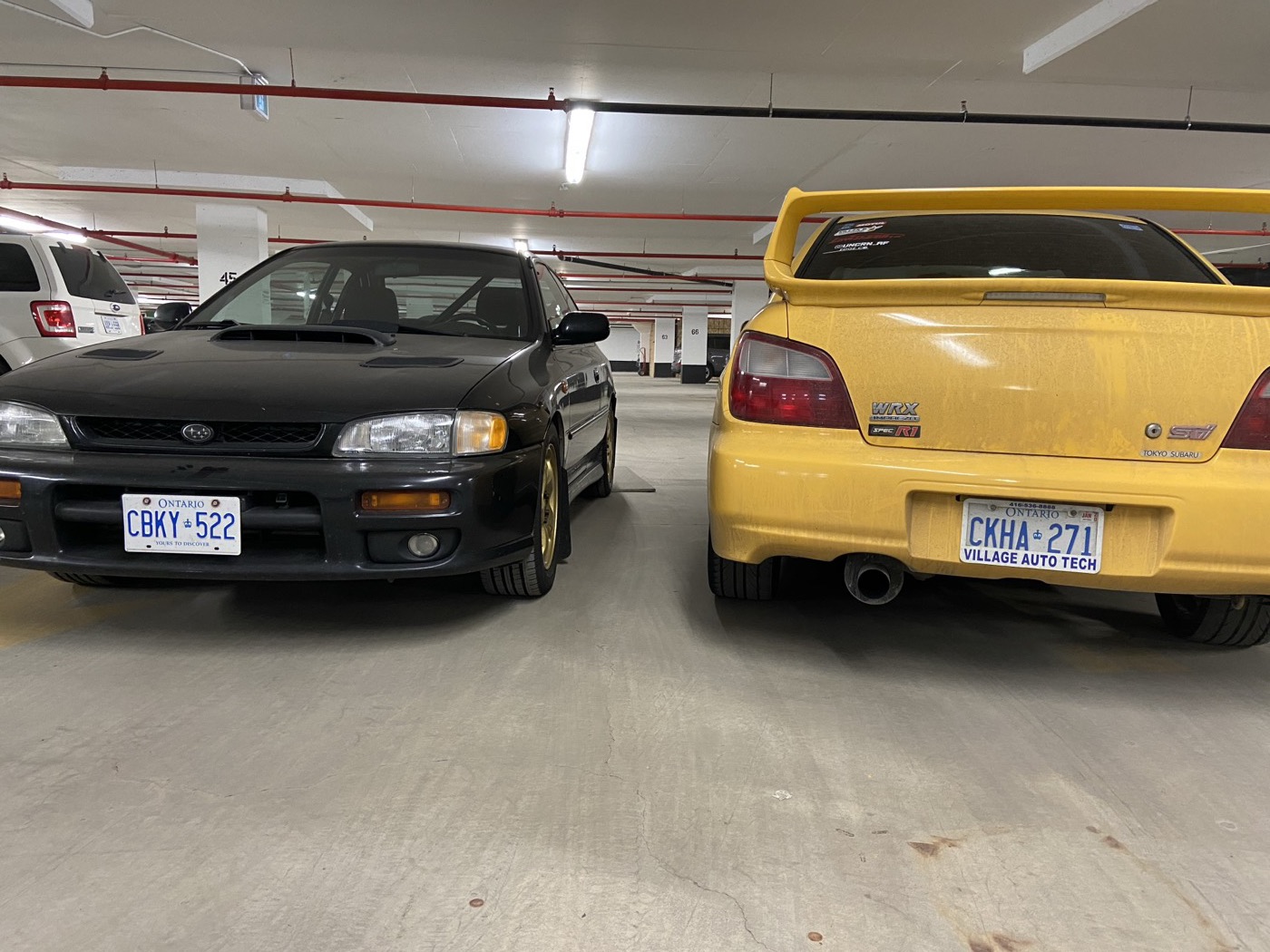 Black 2.5RS parked beside the yellow WRX in an underground garage